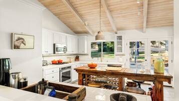 A modern kitchen with white cabinetry, a wooden ceiling, and a large island with various kitchen tools.