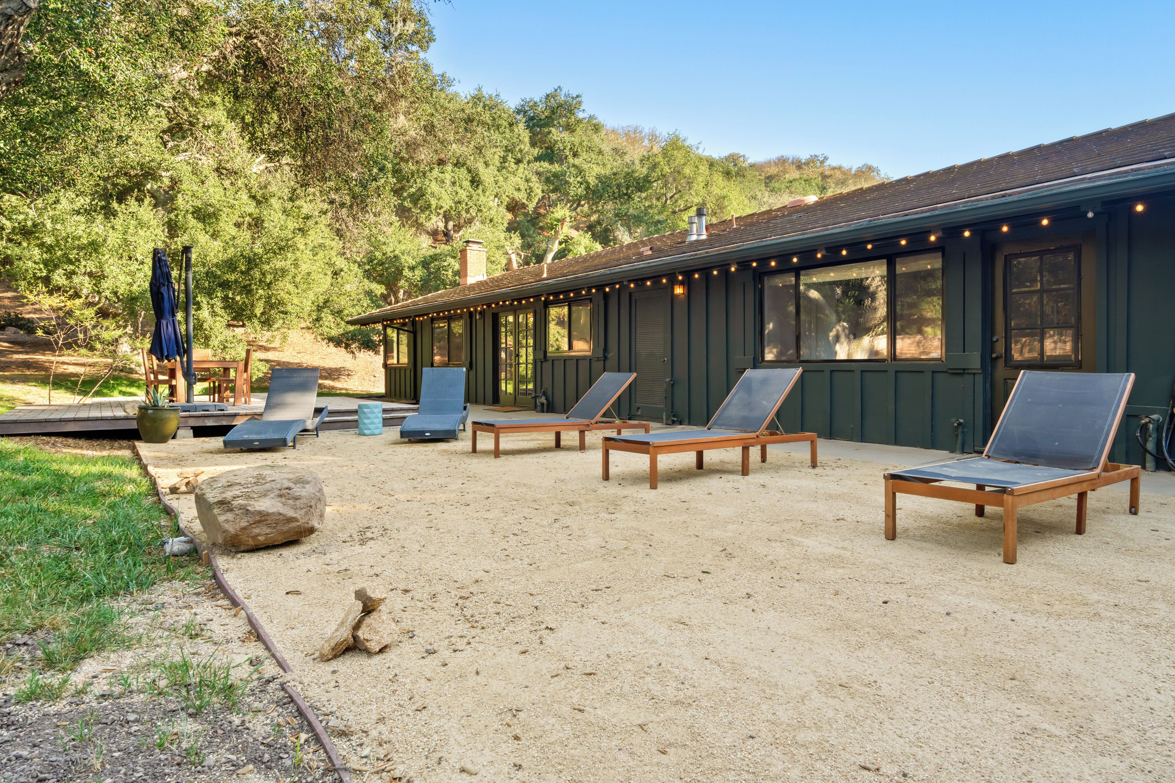 A building with a covered outdoor area, multiple lounge chairs, and a sandy ground.