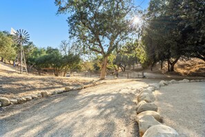 A gravel path with a windmill, trees, and a fenced area. - Rancho de los Venados (Santa Ynez)