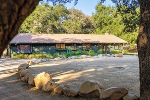 A rustic cabin with a sloped roof, surrounded by a gravel driveway and a rock border. - Rancho de los Venados (Santa Ynez)