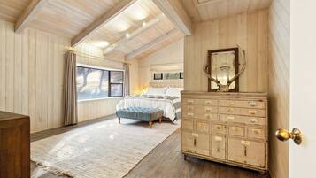 A bedroom with a large window, a bed, a dresser, and a mirror.