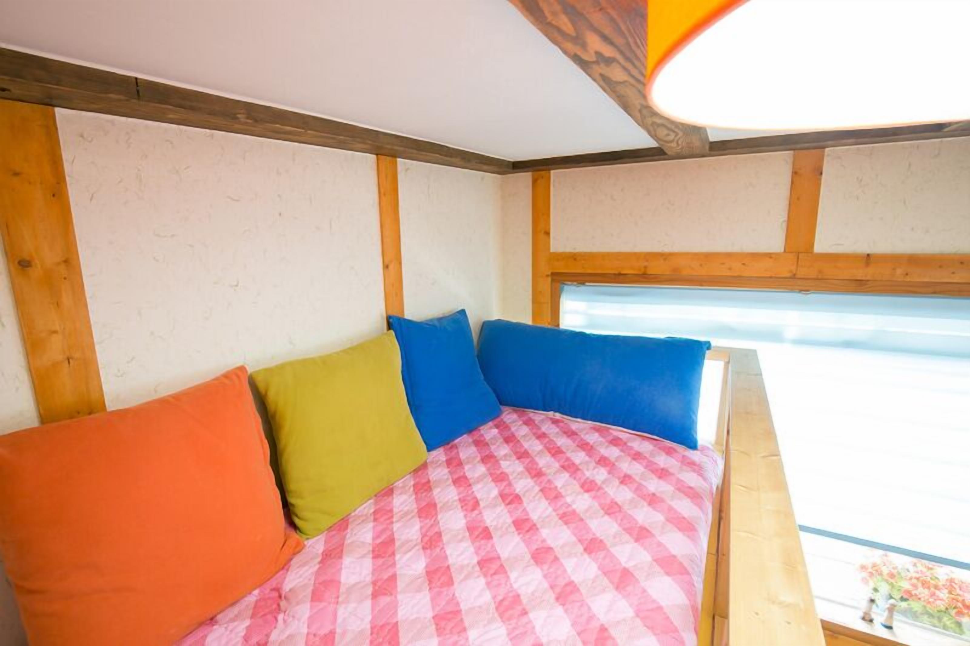 Una cama con almohadas coloridas y una colcha a cuadros, vigas de madera en el techo y una ventana con vistas.