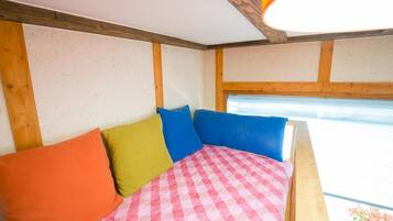 Una cama con almohadas coloridas y una colcha a cuadros, vigas de madera en el techo y una ventana con vistas.