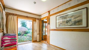 A room with a wooden floor, a stack of folded towels, a door leading outside, and a framed picture on the wall. - Ddlanchae Hanok Stay - Main House (JEONJU)