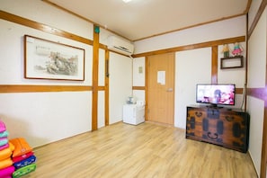 A room with wooden flooring, a television on a wooden cabinet, a framed artwork on the wall, and a white cabinet. - Ddlanchae Hanok Stay - Main House (Jeonju)