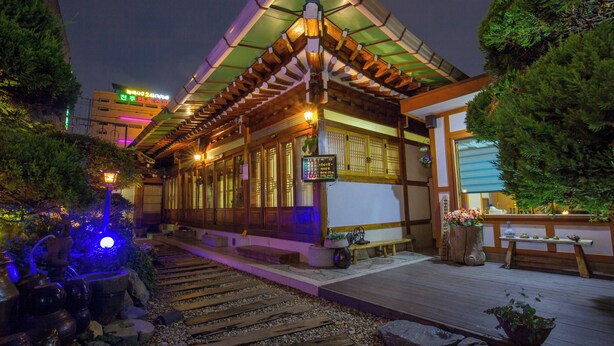 A traditional Japanese building with a wooden structure, a wooden deck, and a stone pathway leading to the entrance. - Ddlanchae Hanok Stay - Main House (JEONJU)