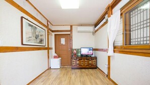 A hallway with wooden flooring, a television on a cabinet, and a door at the end. - Ddlanchae Hanok Stay - Main House (JEONJU)
