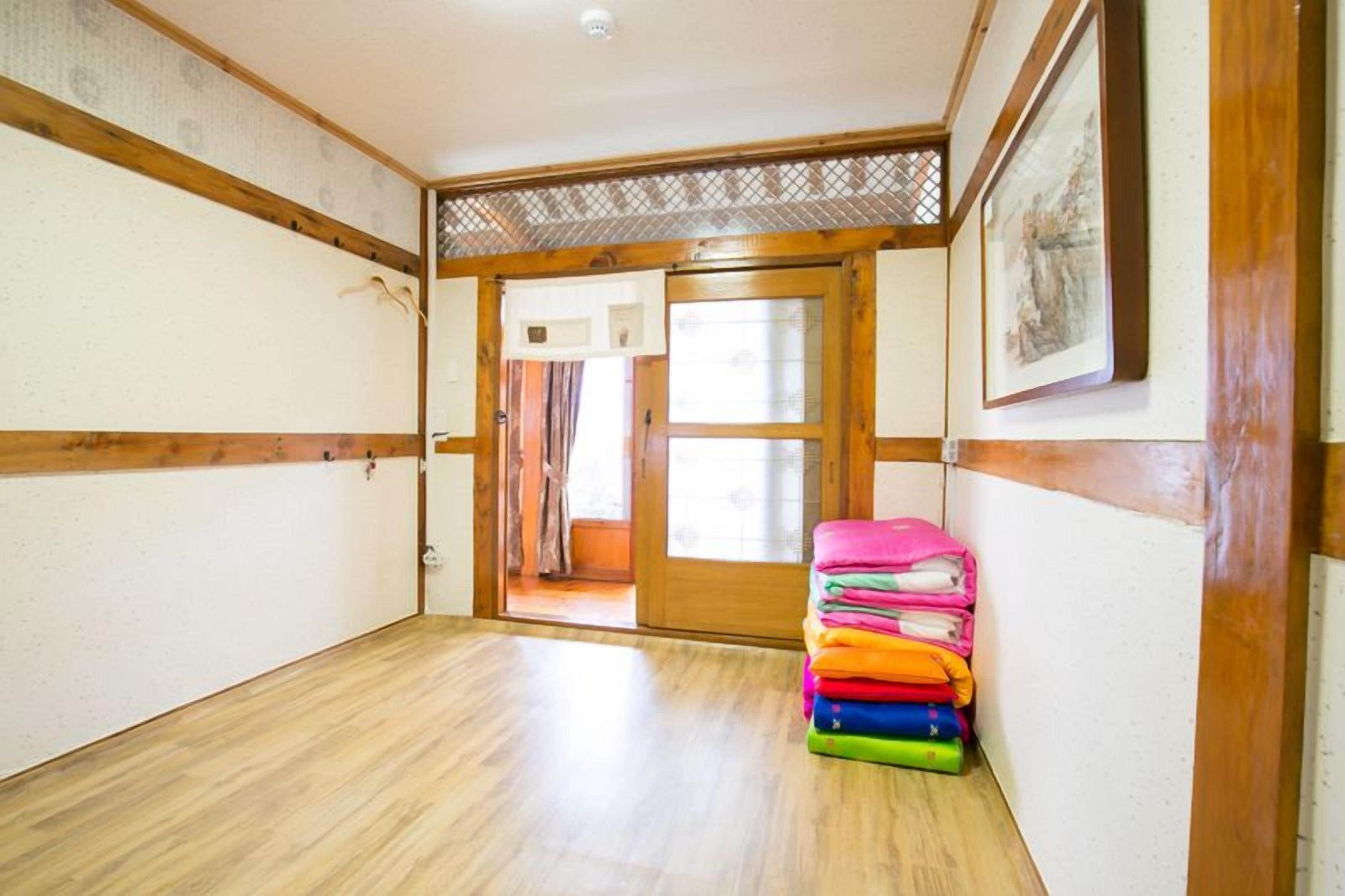 Un pasillo con suelo de madera y una puerta que da a otra habitación. Un montón de toallas de colores se apoya contra la pared.