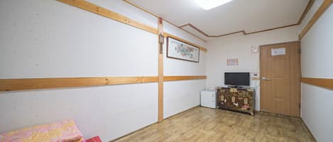 A room with wooden beams on the ceiling, a television, a cabinet with a decorative panel, and a stack of folded towels.