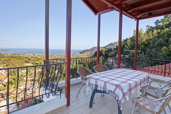Un balcón con mesa y sillas, con vistas a un paisaje costero con casas y árboles.
