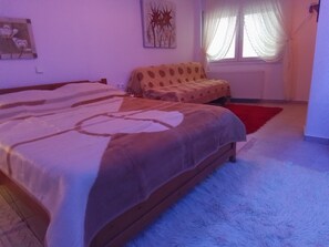 A bedroom with a large bed, a smaller sofa, a red rug, and a window with curtains.
