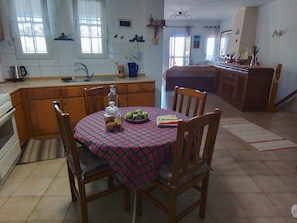 A kitchen with a dining table set for two, a window with curtains, and a tiled floor.