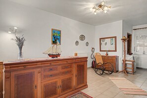 Una habitación con un armario de madera, un sillón mecedora, un modelo de velero pequeño y un espejo en la pared.