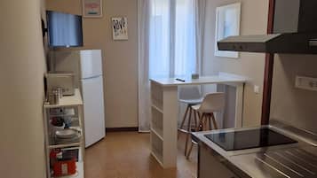 Una cucina compatta con frigorifero, piano cottura e un'area pranzo con sedia e tavolo.