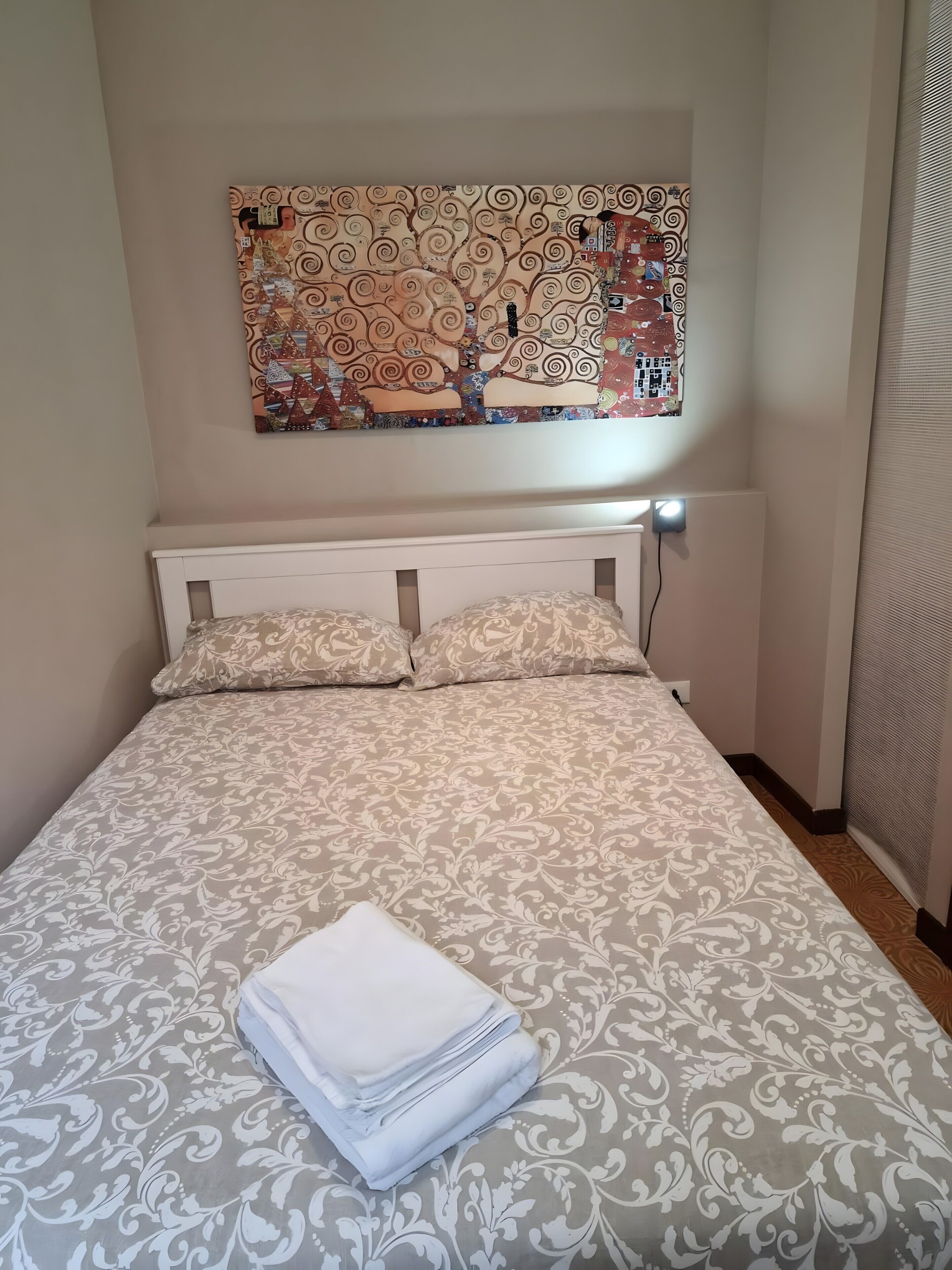 A neatly made bed with a patterned bedspread, a decorative wall hanging above, and a folded white towel on the bed.