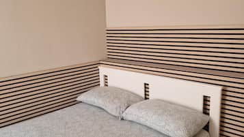 Un letto singolo con una coperta a motivi e due cuscini, appoggiato contro un muro a righe.