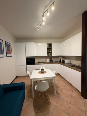 Cocina compacta con armarios blancos, una mesa de comedor con sillas, microondas y cafetera.