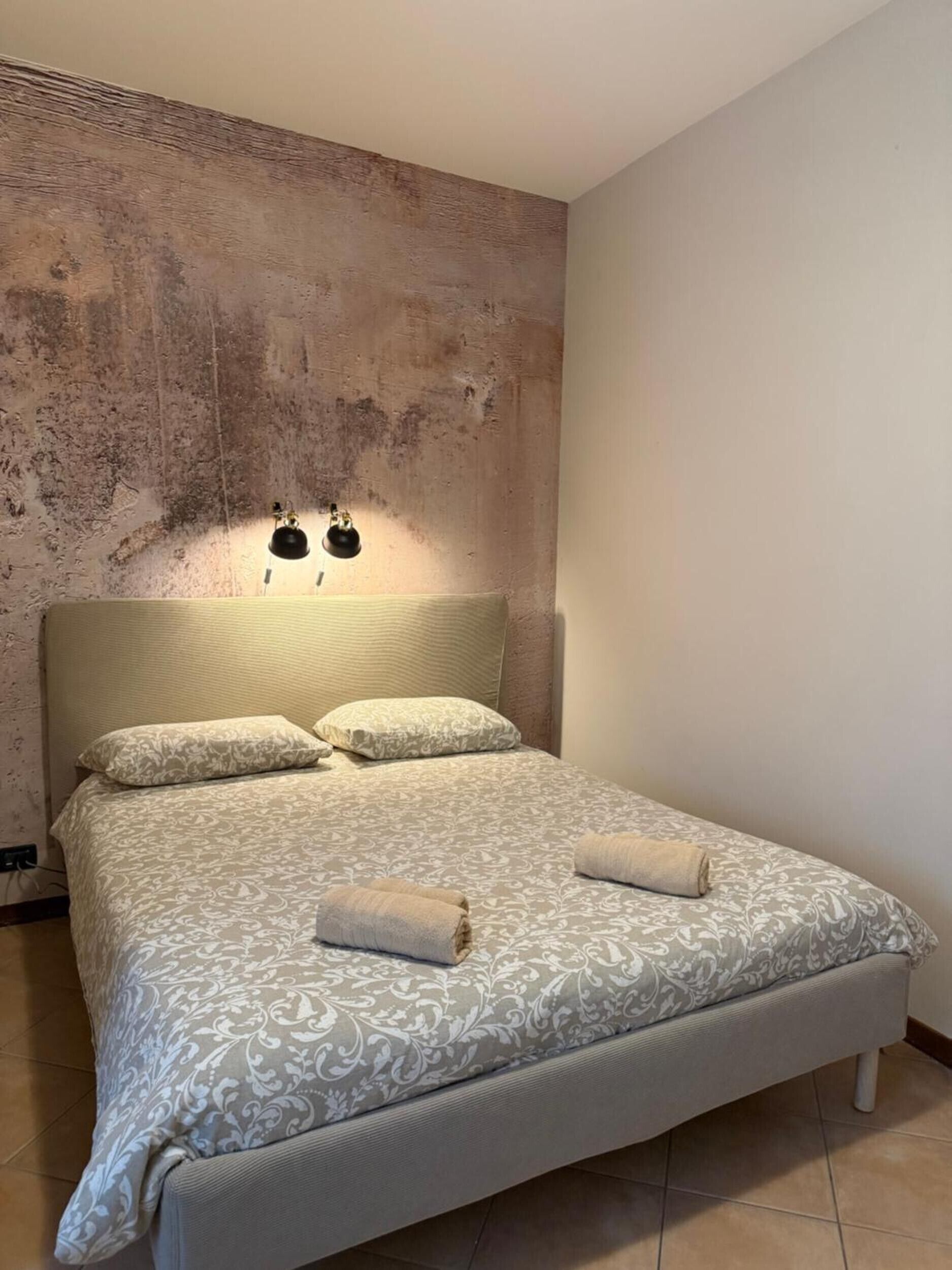 Ein Schlafzimmer mit einem Bett, zwei Wandleuchten und einer strukturierten Wand.