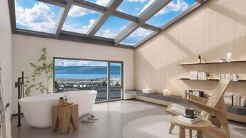 A modern bathroom with a skylight, a bathtub, a wooden side table, and a view of the sea.