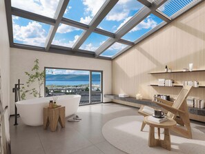 Un baño moderno con tragaluz, una bañera, una mesita de madera y vistas al mar.