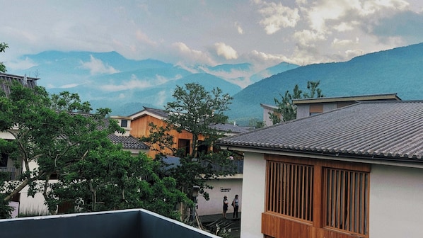 Casas japonesas tradicionais com fachadas de madeira e telhados de telha, com montanhas e um céu nublado ao fundo.