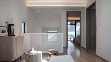 Un interior moderno con un mueble de madera, un taburete redondo de madera y un pouf blanco.