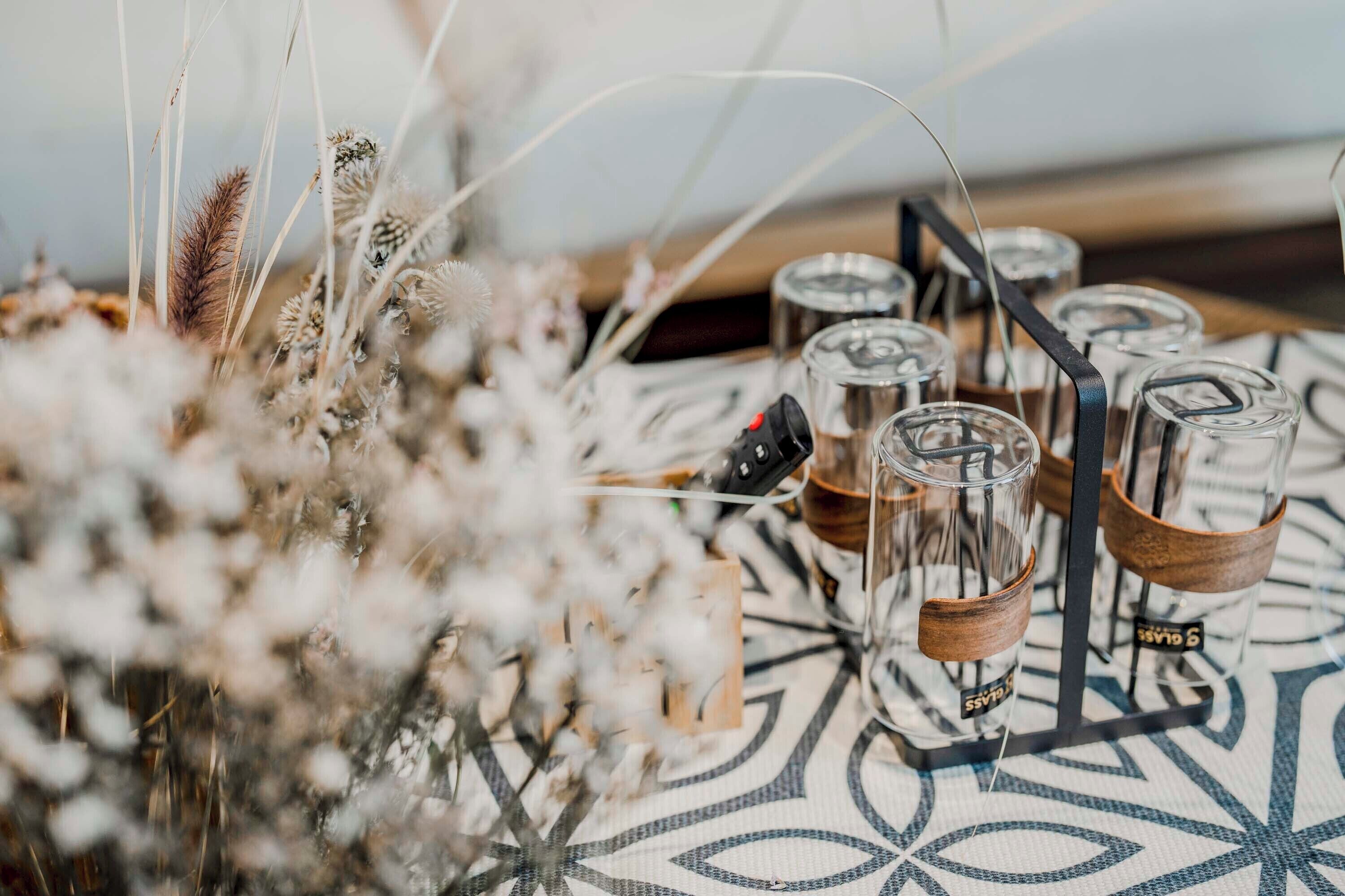 Une table avec des verres en verre transparent, dont certains sont ornés de bandes en bois, et une nappe à motifs.
