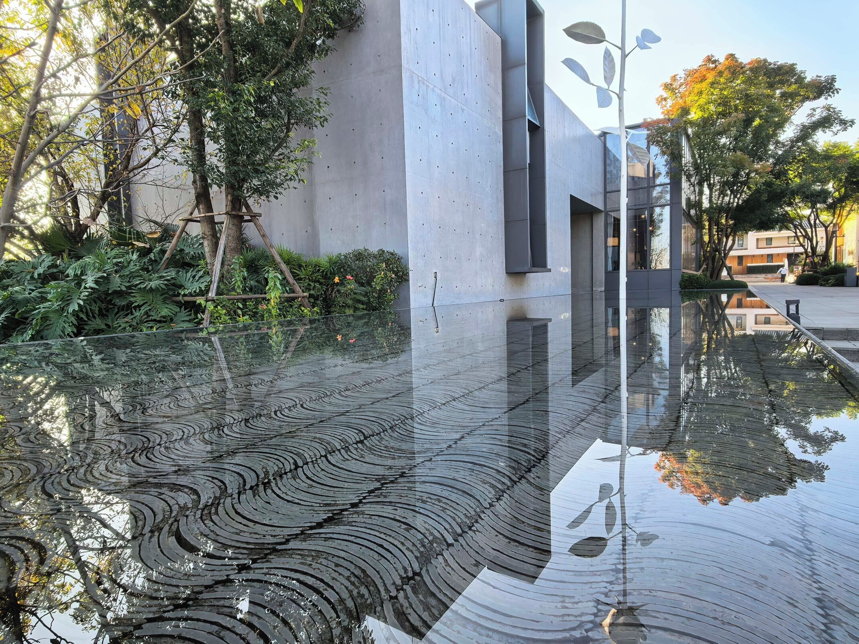 A modern building with a glass facade reflecting trees and sky.