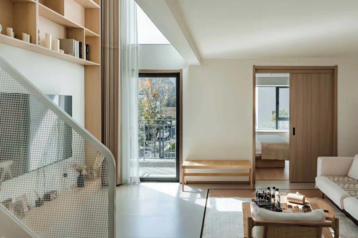 Uma sala de estar moderna com escada, sofá, mesa de centro e vista para o exterior.