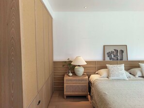 Un dormitorio con cama, mesita de noche, lámpara y una obra de arte enmarcada en la pared.