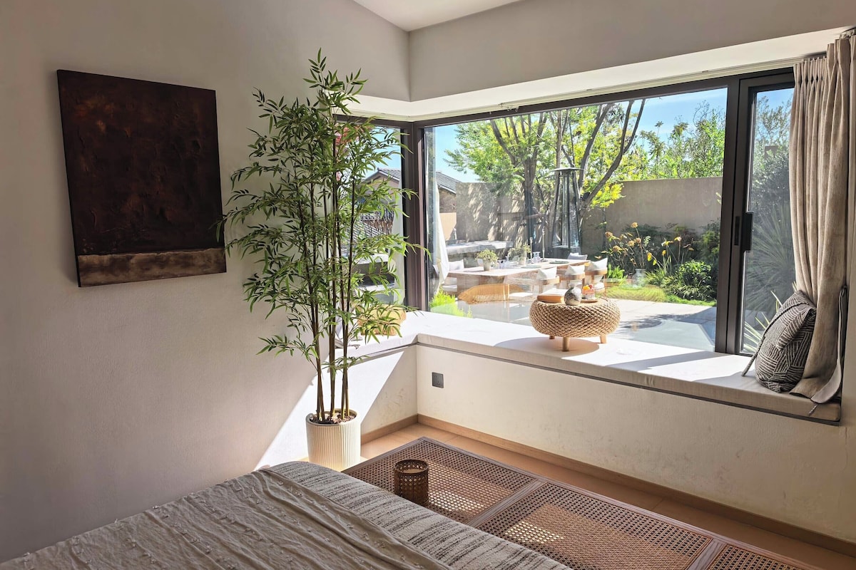 Quarto com uma grande janela, planta em vaso, cama e vista para o exterior.