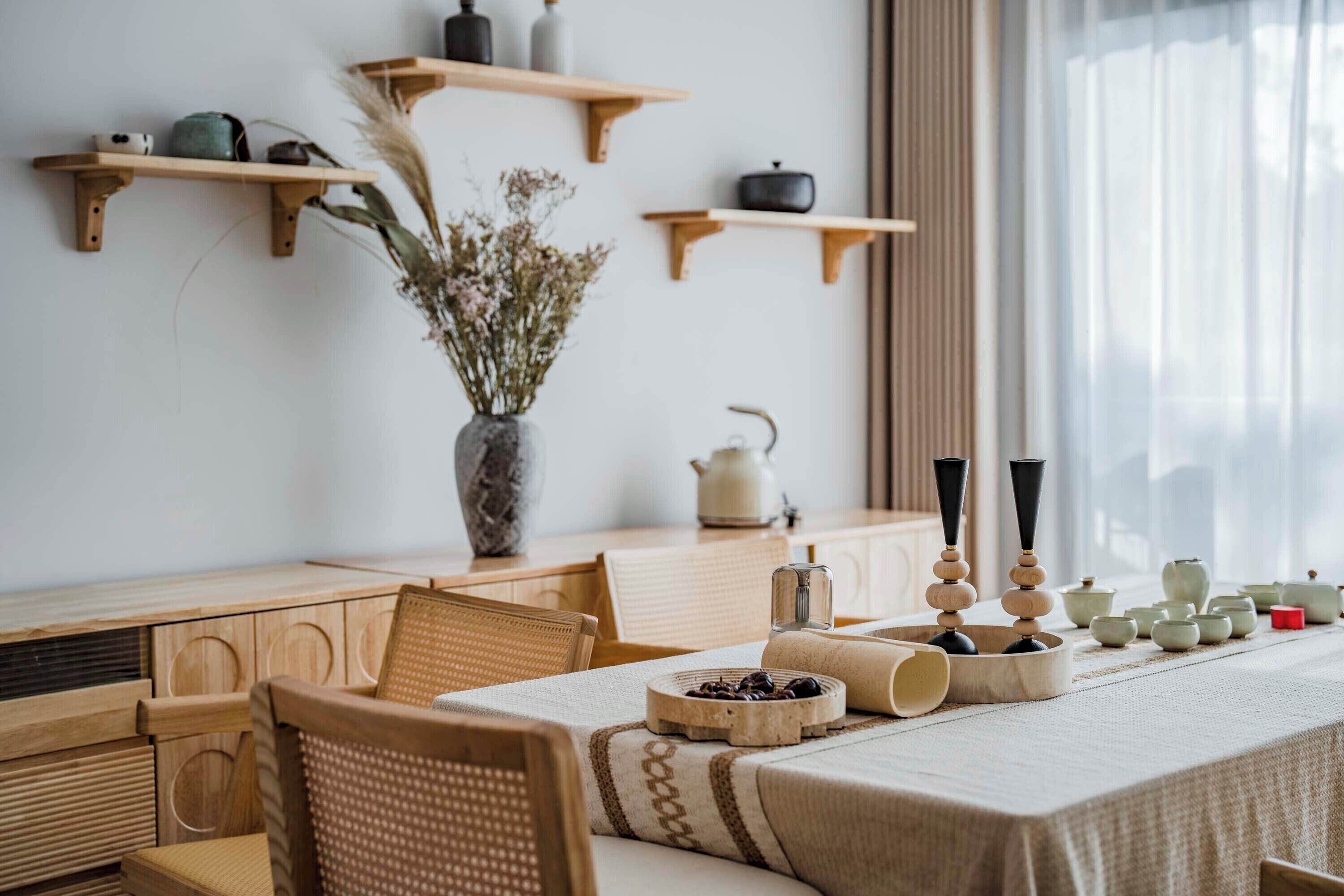 A dining area with a wooden table, chairs, and a vase with dried flowers.