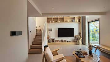 A modern living room with a staircase, a flat-screen TV, and a large window.