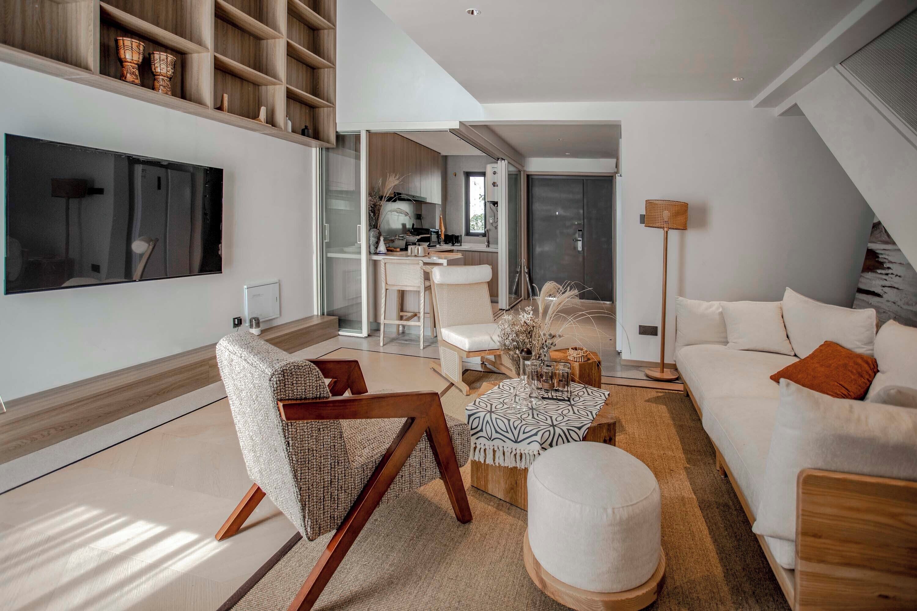 A modern living room with a large flat-screen TV, a sofa, a coffee table, and a dining area with a kitchen in the background.