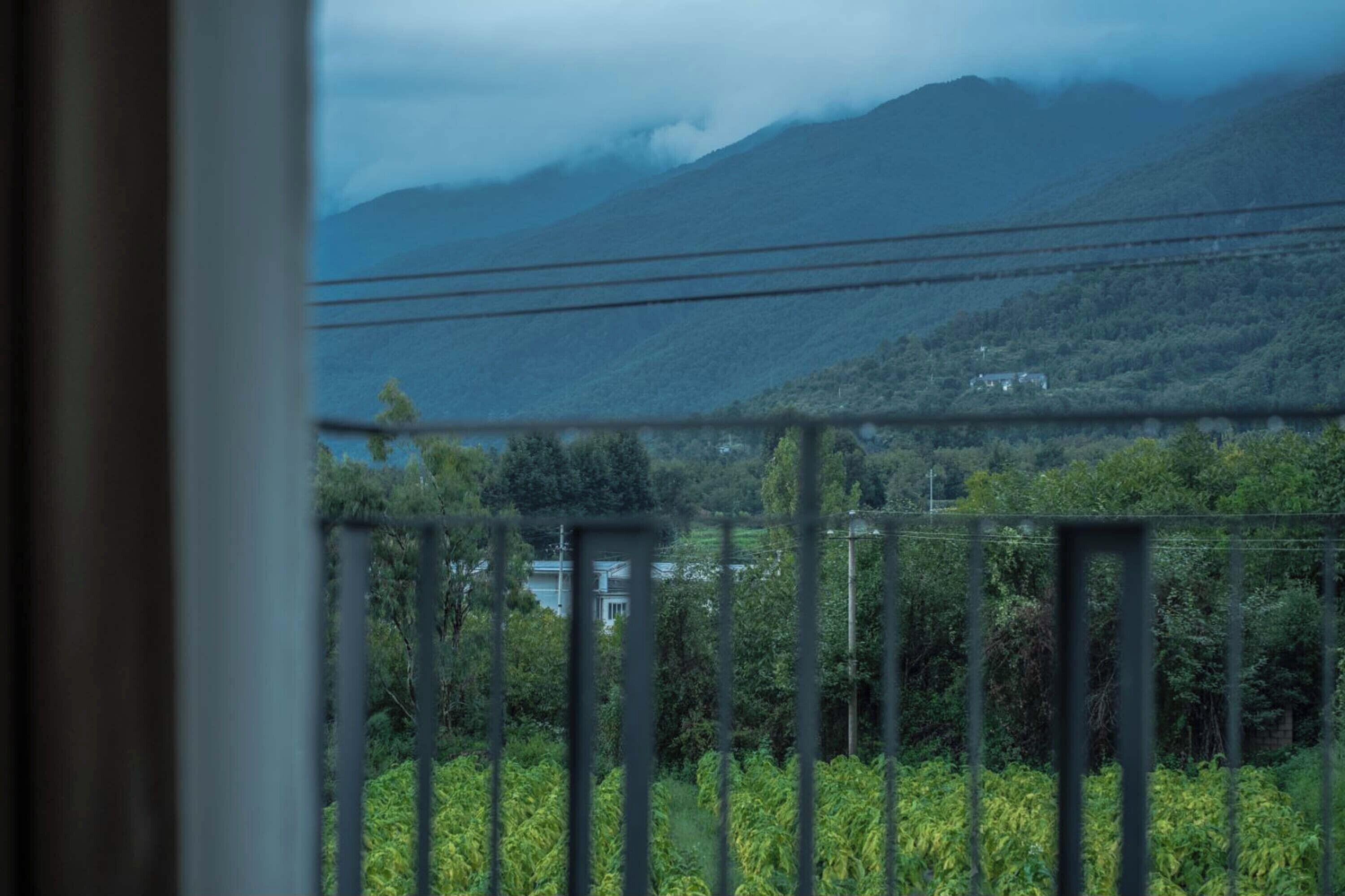 A view of a mountainous landscape with a house and greenery in the foreground.