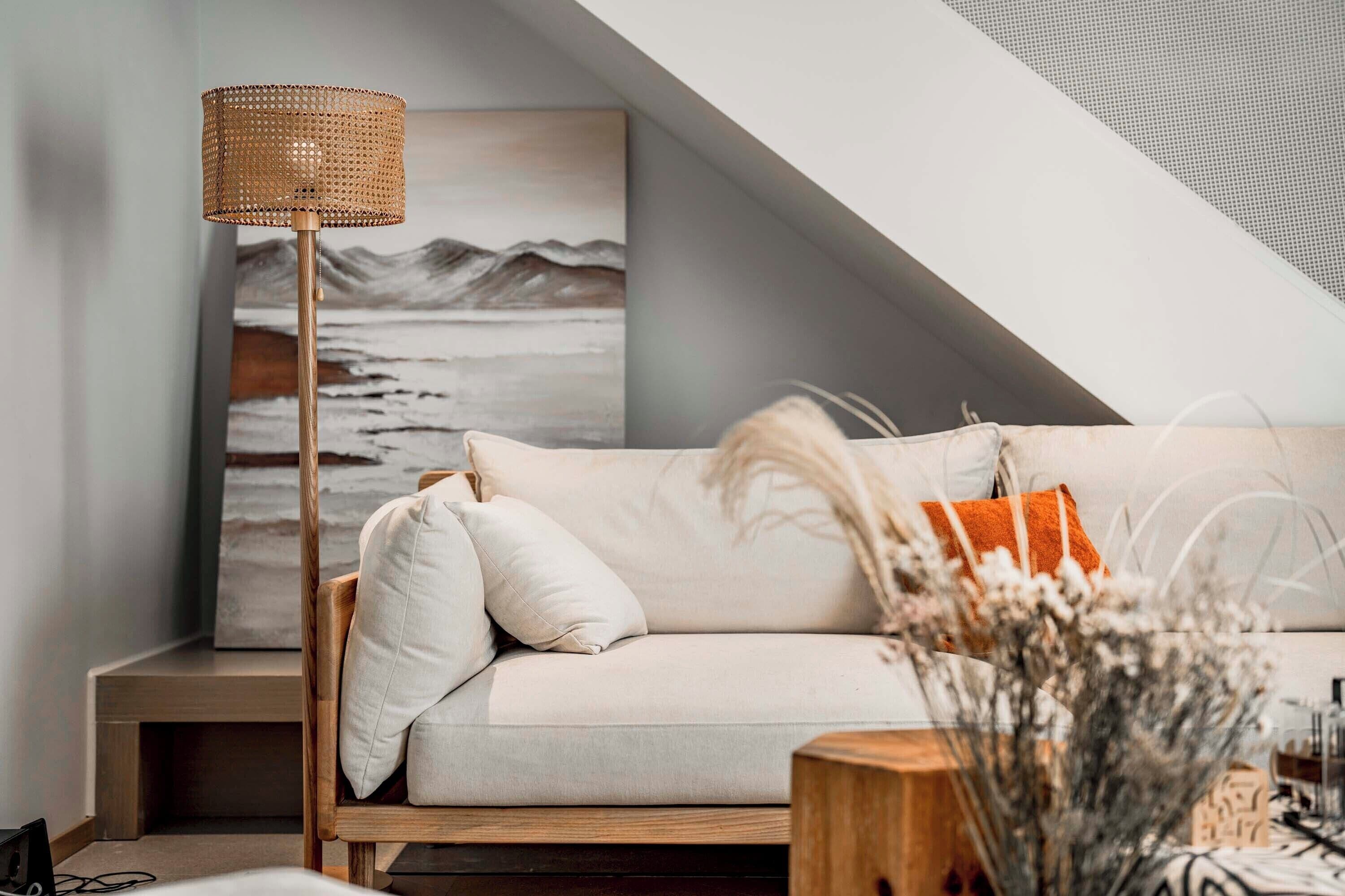 A modern living room with a white sofa, a wooden floor lamp, and a painting of a landscape.