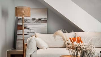 A modern living room with a white sofa, a wooden floor lamp, and a painting of a landscape.