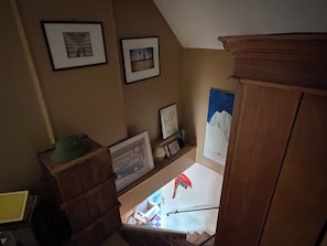 Eine Treppe mit hölzernem Geländer, ein grüner Hut auf einer Kiste und gerahmte Bilder an den Wänden.