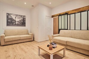 A living room with two beige sofas, a wooden coffee table, and a framed black and white cityscape picture on the wall. - Superb apartment center of Paris (Paris)