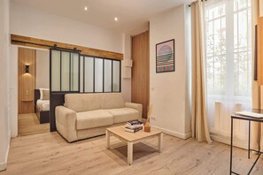 A modern living room with a sofa, a coffee table with books, a window with curtains, and a wooden floor. - Superb apartment center of Paris (Paris)