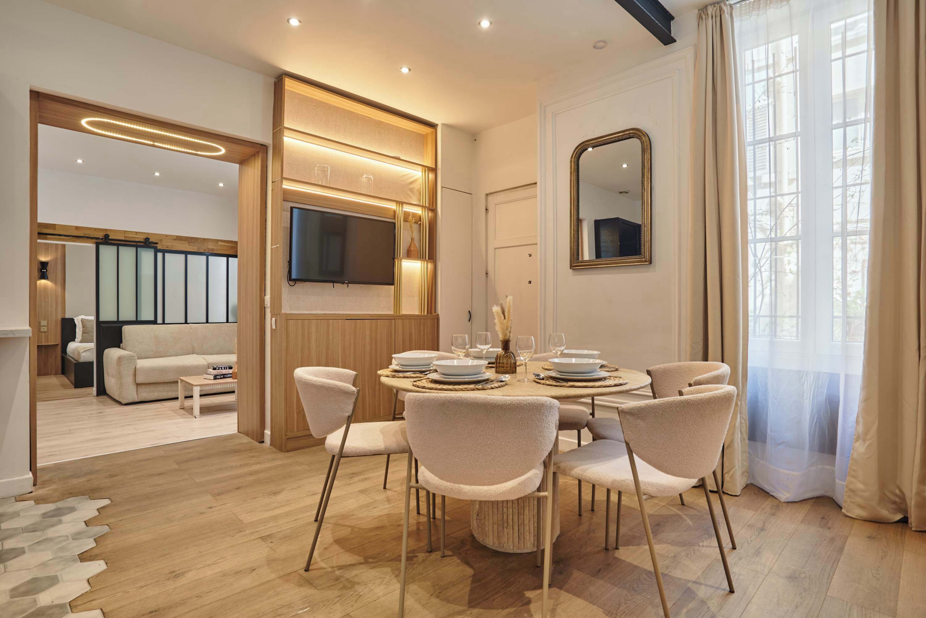 A modern dining area with a round table, six chairs, and a television mounted on the wall.