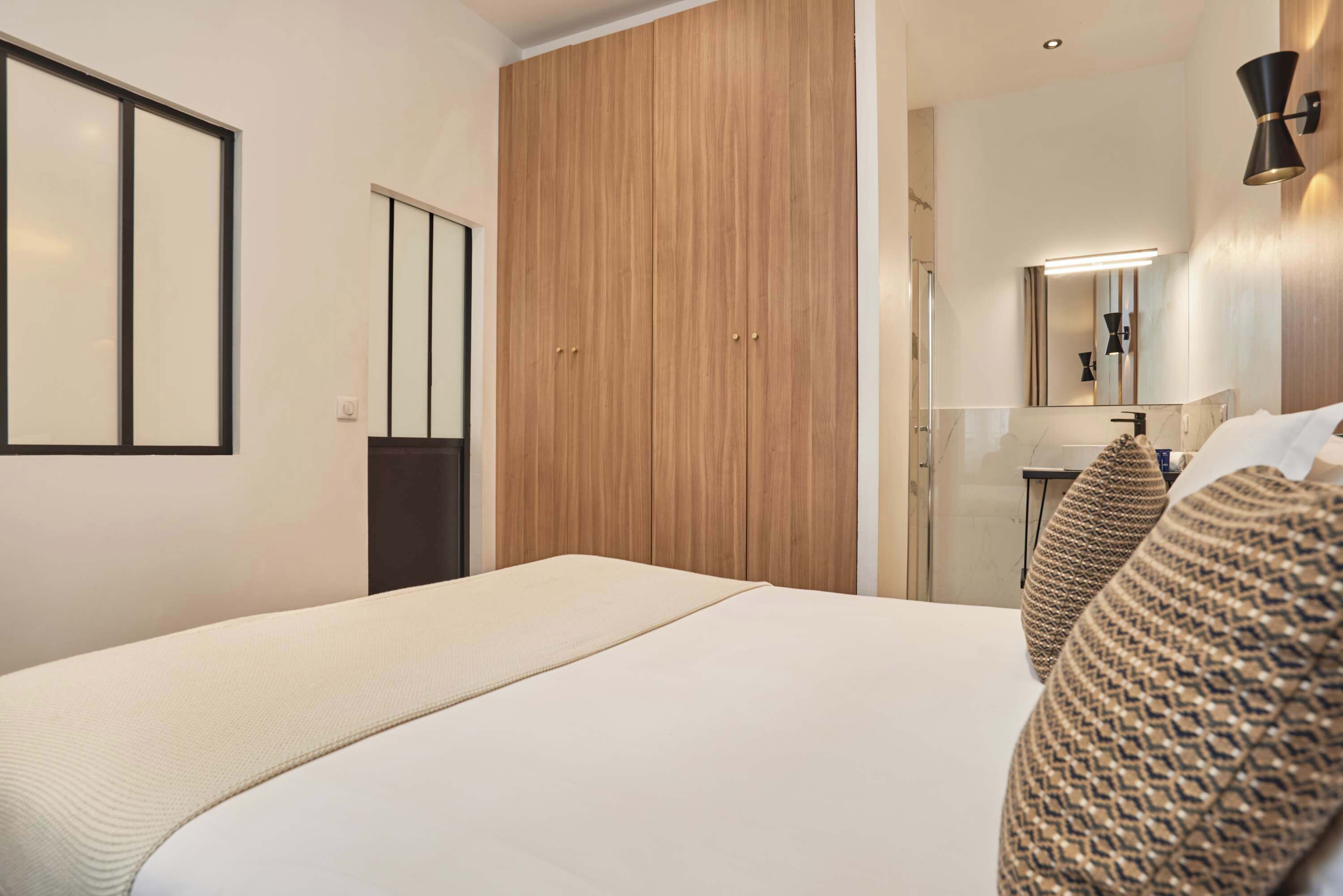A hotel room with a bed, wooden wardrobe, and a bathroom with a mirror and towel rack.