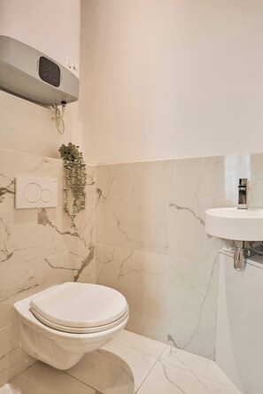 A bathroom with a toilet, a wall-mounted heater, a small plant, and a sink with a mirror. - Superb apartment center of Paris (Paris)