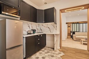 A modern kitchen with dark cabinets, a stainless steel refrigerator, and a marble backsplash. - Superb apartment center of Paris (Paris)