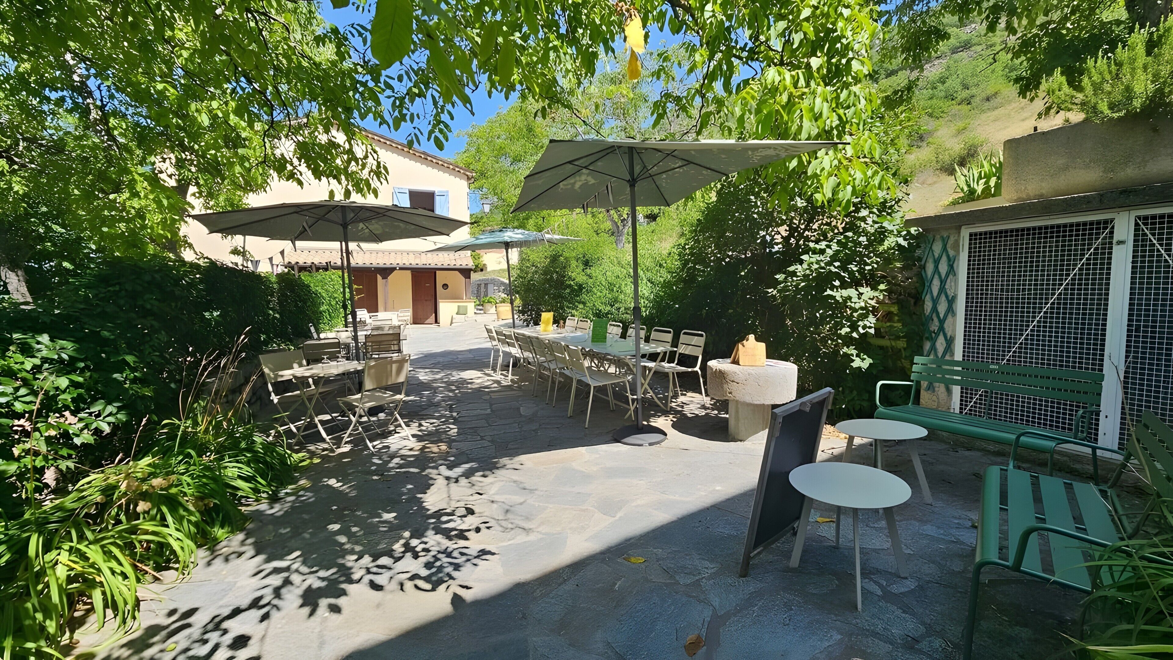 Une terrasse extérieure avec des tables et des chaises, des parasols et des plantes.