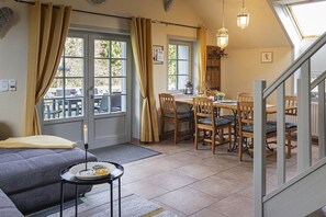 A cozy room with a sofa, dining table, chairs, and a staircase. - "To the forest disc" (Rammenau)