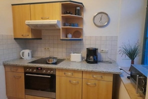 A compact kitchen with wooden cabinets, a built-in oven, a coffee maker, and a clock on the wall. - Marina at the sailing harbor (Karlshagen)