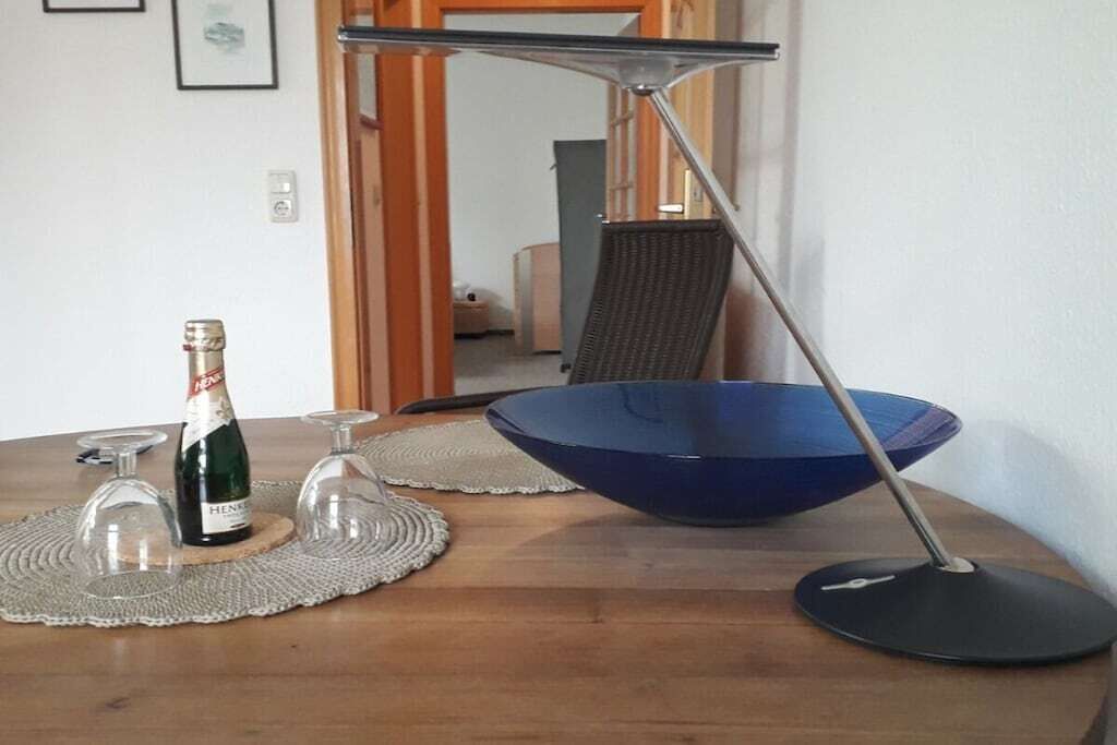 Una mesa de comedor con una botella de champán, dos copas de vino y un tazón azul sobre un mantel tejido.