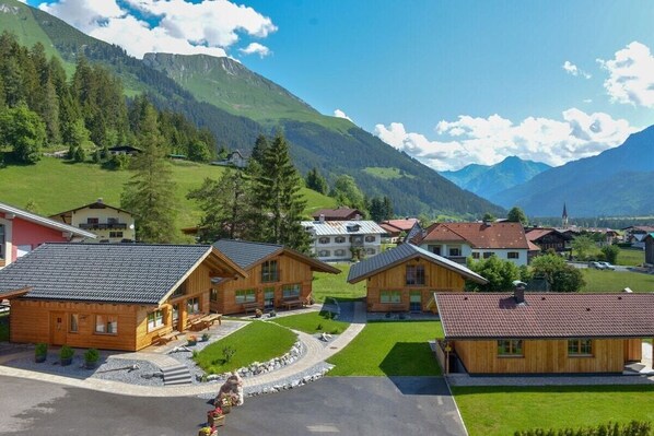 A cluster of wooden cabins with a mountain backdrop, a paved driveway, and a small parking area.