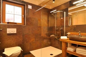 A modern bathroom with a glass-enclosed shower, a wooden vanity with a stone sink, and a toilet with a towel on it.